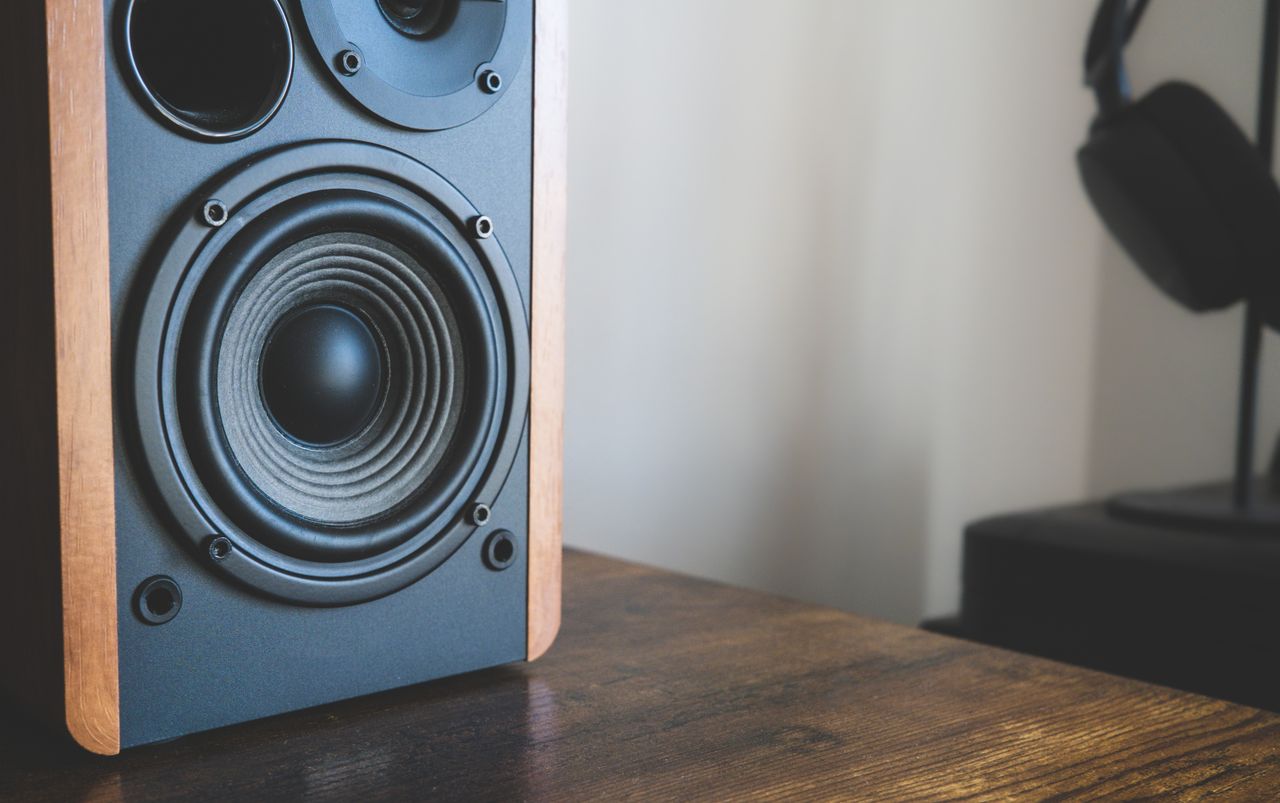 Close-up shot of a speaker and headphones on a wooden desk, highlighting modern audio technology.